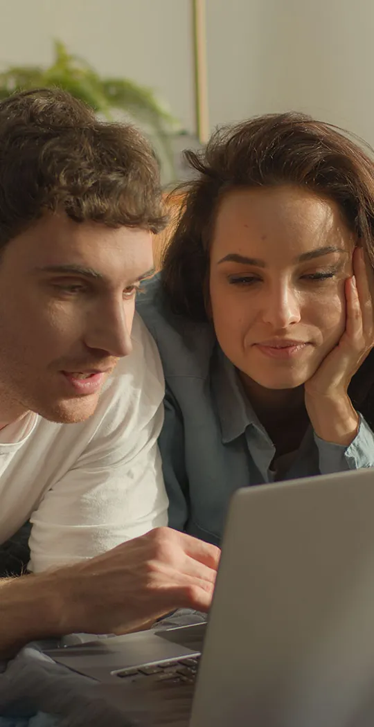 Junges Paar liegt im Bett und ist am Laptop. 